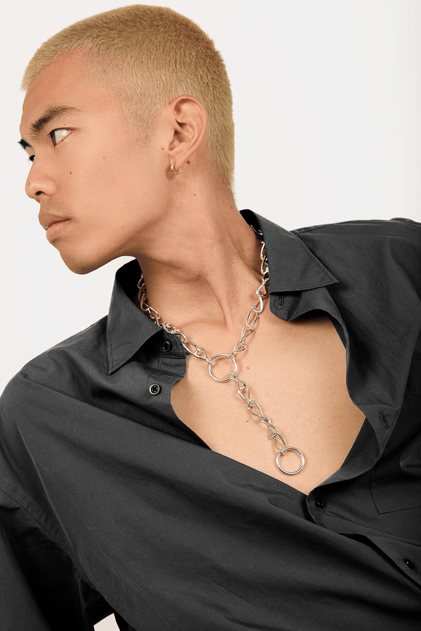 Model in an open black shirt wearing a necklace of large interlocking loops in silver